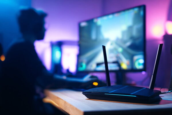 Gaming-Router sorgt für niedrigen Ping und stabile Verbindung Gaming-Router neben PC-Setup mit visualisierten Datenwegen für niedrigen Ping und stabile WLAN-Verbindung.