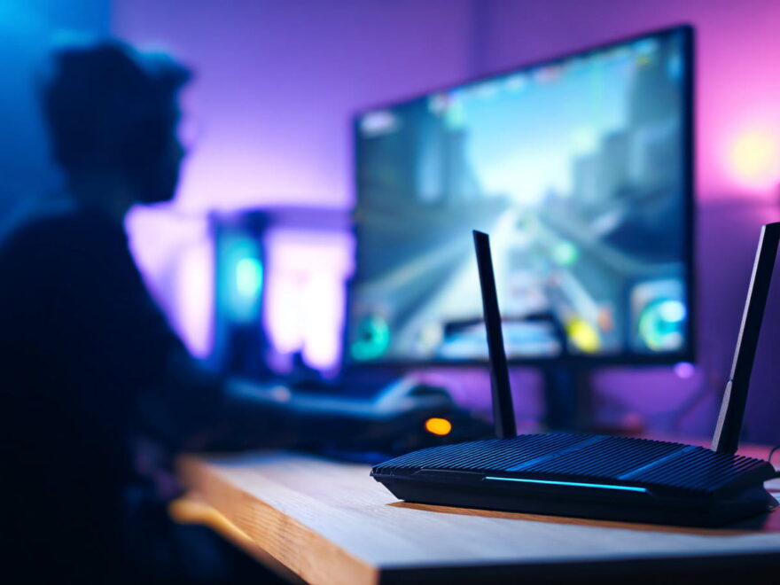 Gaming-Router neben PC-Setup mit visualisierten Datenwegen für niedrigen Ping und stabile WLAN-Verbindung.